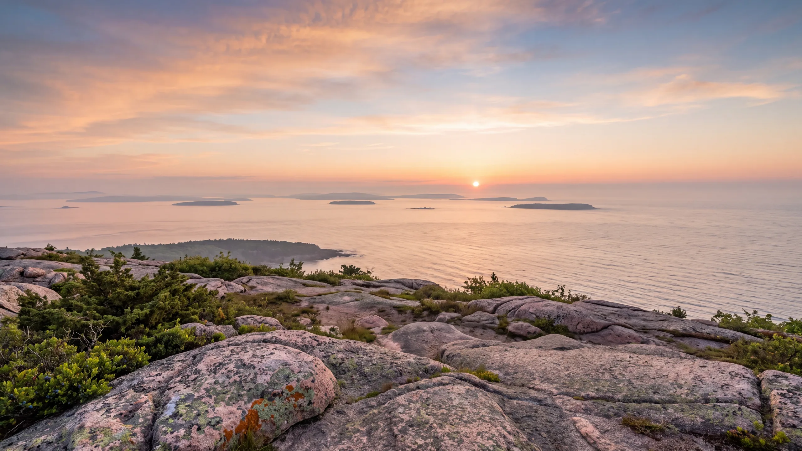 AI-created interpretation of sunrise from Cadillac Mountain in Acadia, with pink granite, island silhouettes, a calm Atlantic sea, and a peach sky.