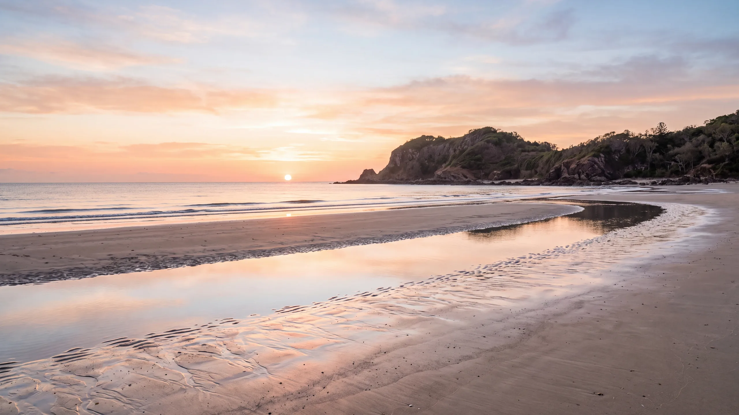 AI-created interpretation of Cape Hillsborough in Queensland at sunrise, with coral light reflected on wet beach sand, a calm Coral Sea and a dark coastal headland.