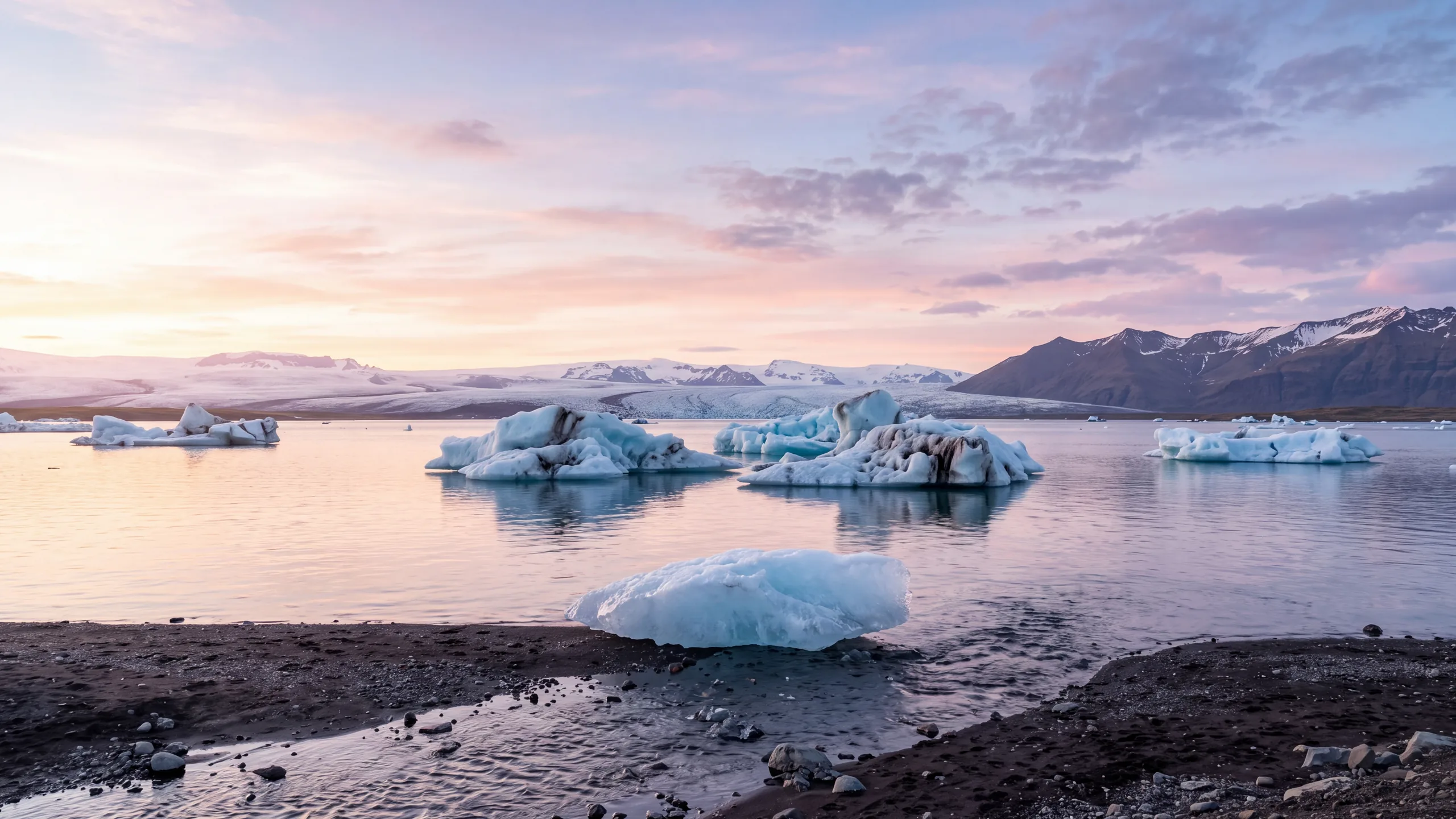 AI-created interpretation of Jökulsárlón in Iceland at sunset, with blue icebergs floating on a calm glacier lagoon and delicate pink light above the distant ice and mountains.