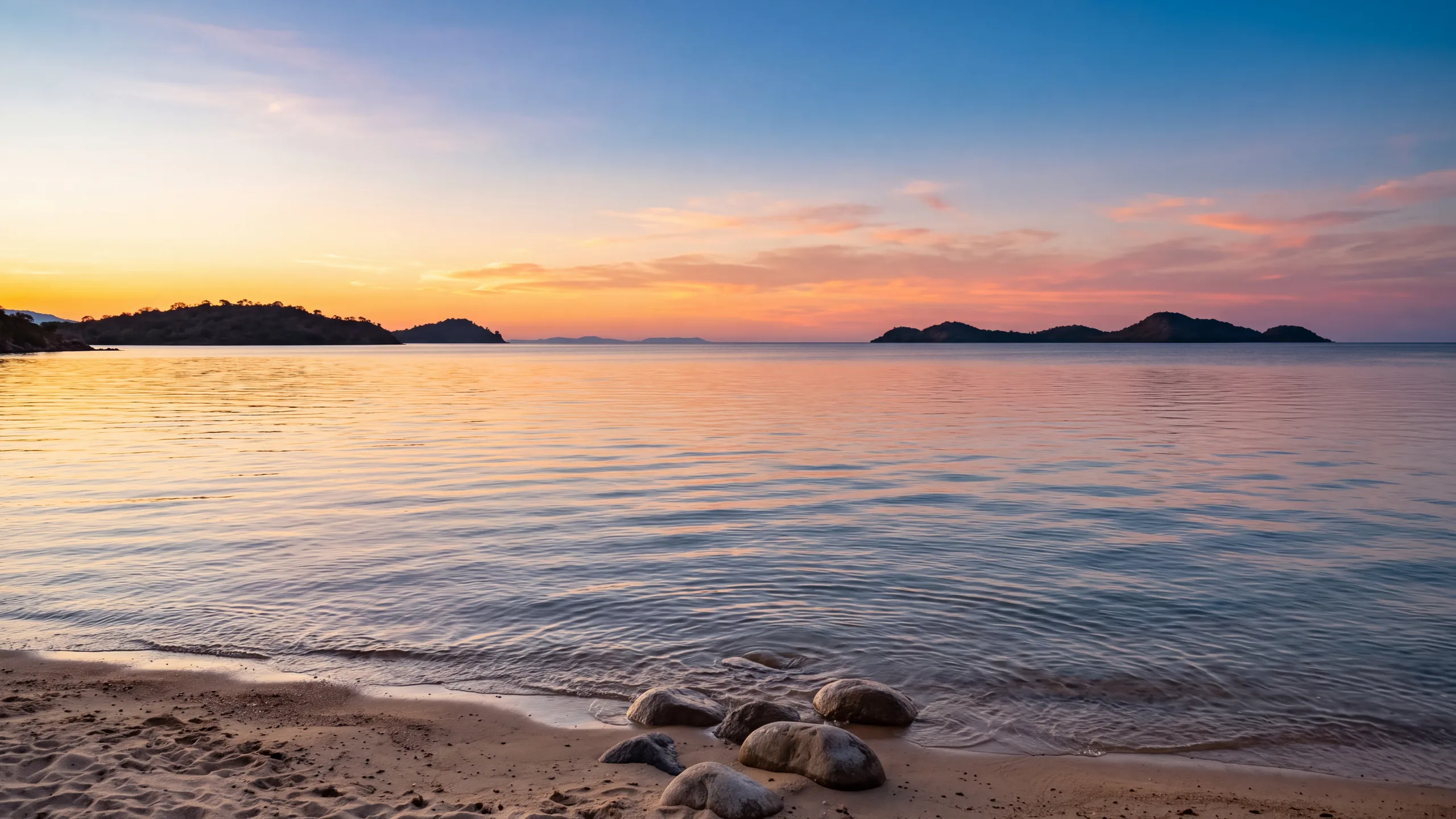 AI-created interpretation of Lake Malawi near Cape Maclear at sunset, with warm amber light across gently rippled freshwater, a sandy shore and distant wooded islands.