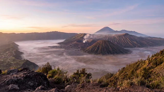 AI-created interpretation of Mount Bromo in East Java at sunrise, with a softly steaming crater, the ribbed cone of Mount Batok and distant volcanic slopes above a misty caldera.