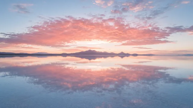 AI-created interpretation of Salar de Uyuni in Bolivia at sunset, with a shallow layer of water mirroring pink clouds and a distant low mountain horizon.