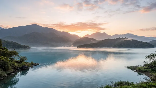 AI-created interpretation of Sun Moon Lake in Taiwan at sunrise, with a peach dawn above layered green mountains and soft mist drifting over blue water.