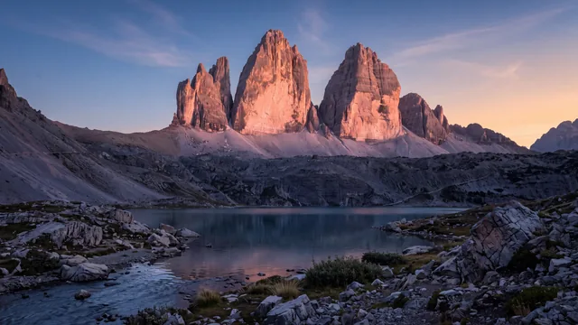 AI-created interpretation of the towers above Base Torres lagoon in Torres del Paine, Chile, at sunrise, with rose-gold light on the peaks, blue-shadowed rock and reflections in calm water.
