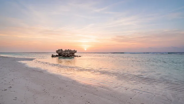 AI-created interpretation of Watamu in Kenya at sunrise, with pale sand, shallow reef-protected water and a soft peach glow across the Indian Ocean.